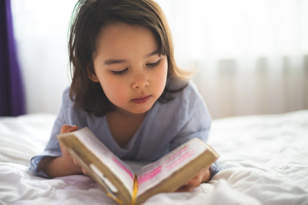 Little girl reading from bible while she is in bed in the morning